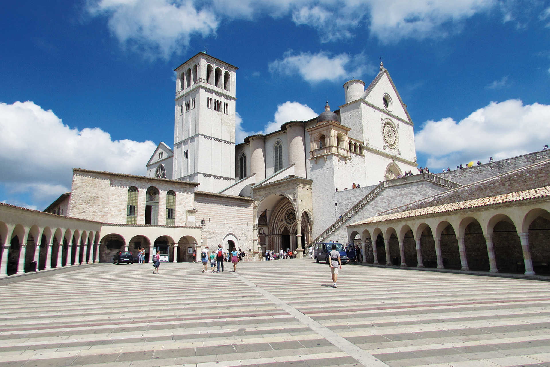 Weitblick auf die mittelalterliche Stadt Assisi mit der imposanten Basilika San Francesco am Hang des Monte Subasio, umgeben von grüner Hügellandschaft.