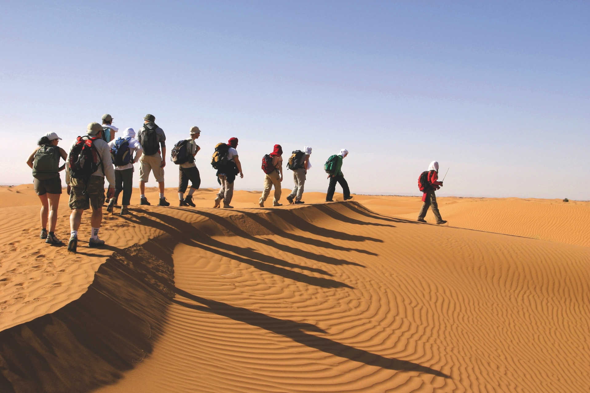 Gruppe von Menschen mit Rucksäcken wandert auf einer Sanddüne durch die Wüste Sahara