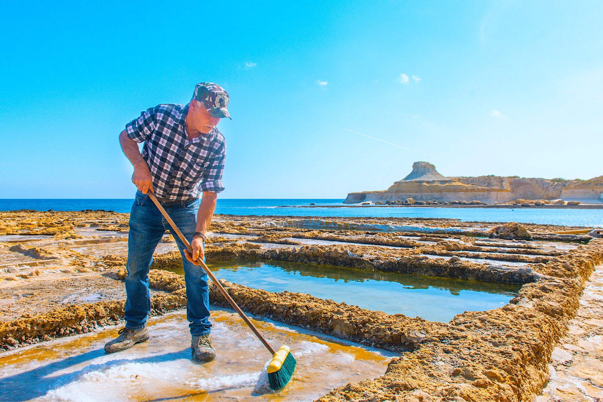 Ein Mann schöpft Meerwasser aus traditionellen Salinen auf Gozo