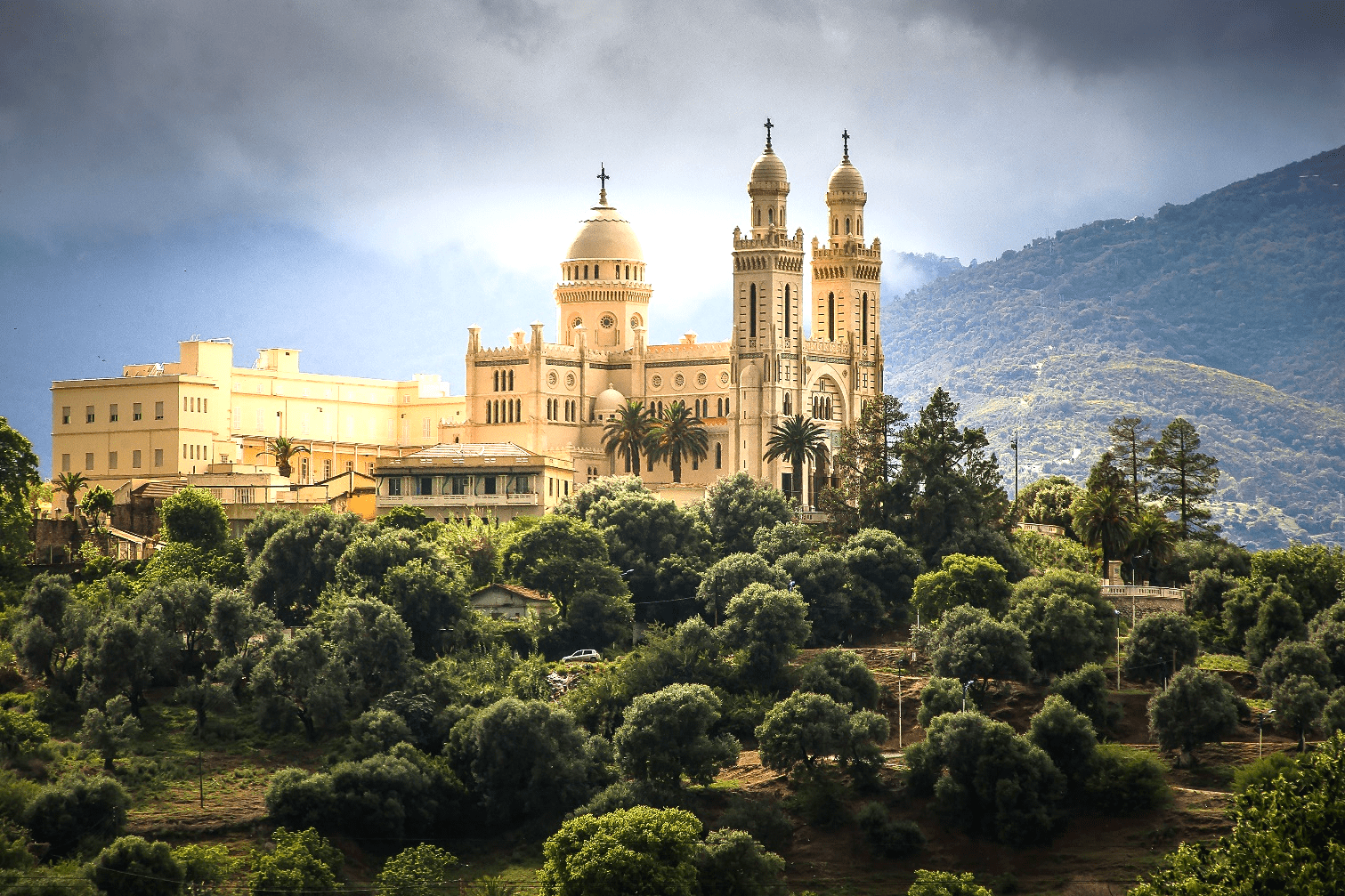 Große weiße Basilika mit Kuppeln und Türmen auf grünem Hügel