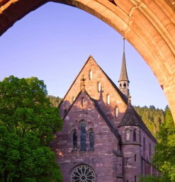 Blick durch Steinbogen auf die rote Sandsteinkirche mit Turm
