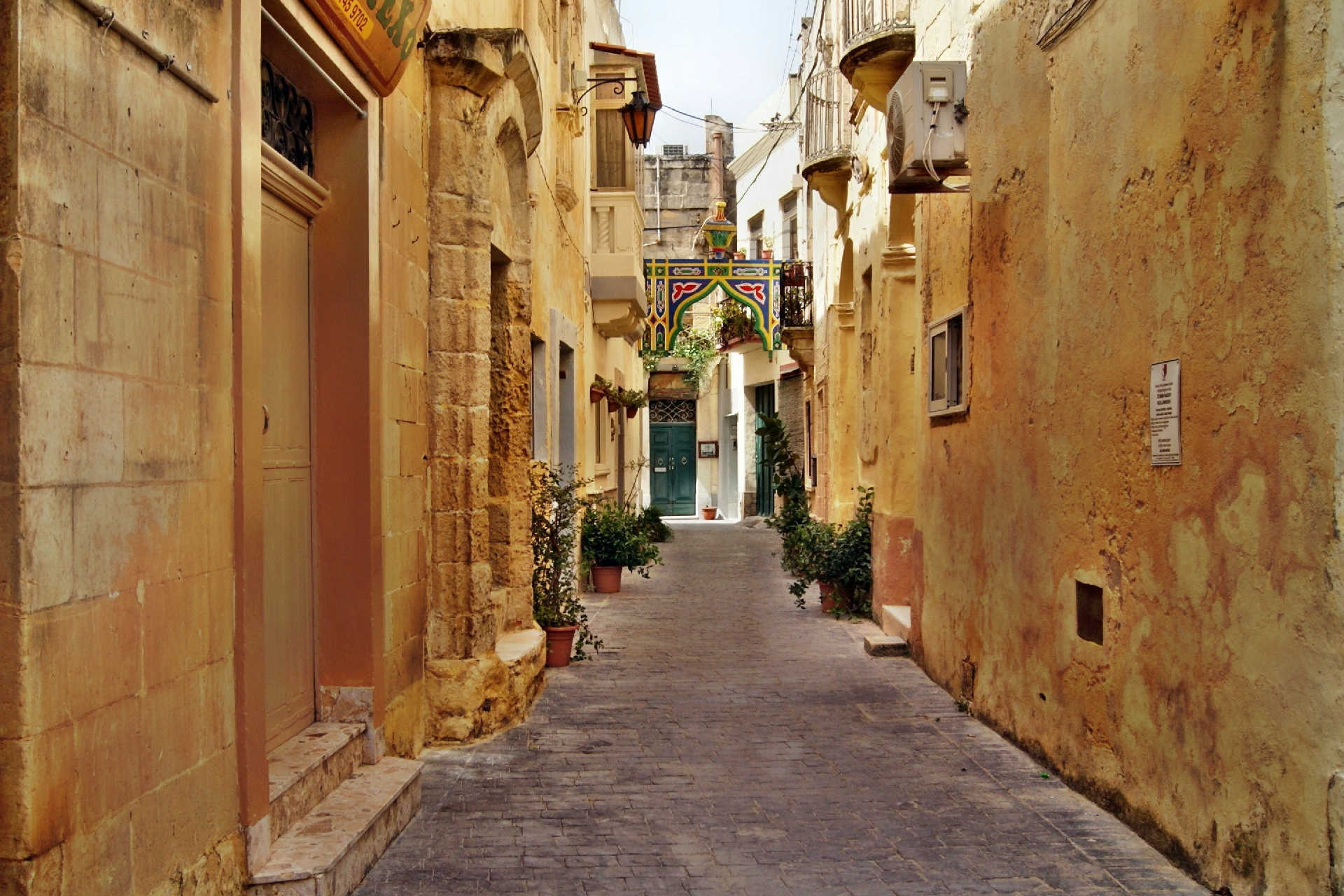 Schmale Gasse mit Topfpflanzen und geschmücktem Bogen in Vittoriosa auf Malta