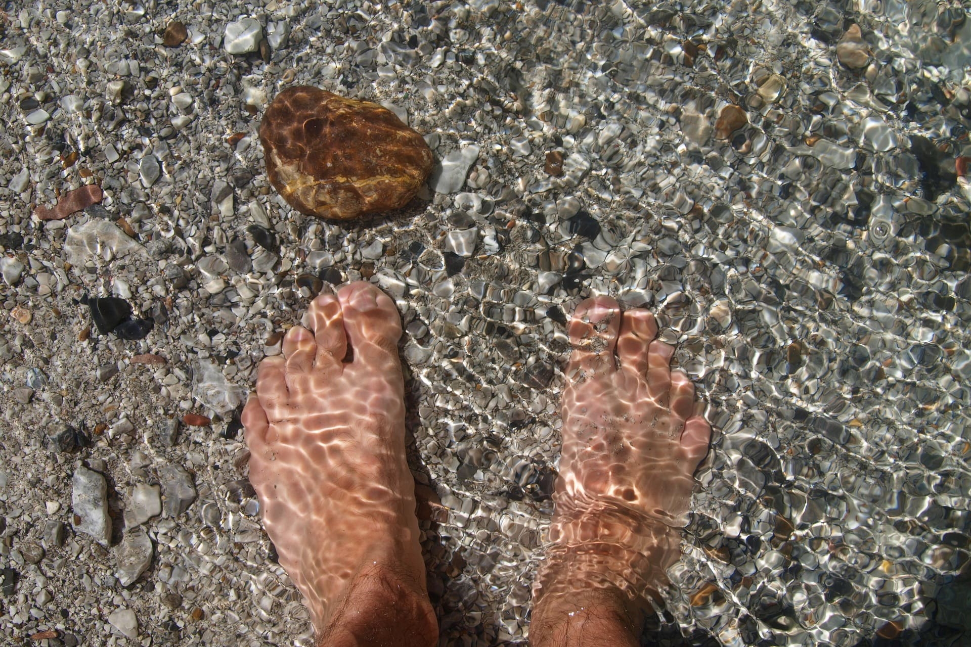 Barfuß im flachen Bach mit Kieseln und Sonnenspiegelungen