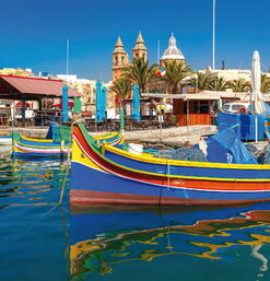 Bunte Fischerboote im Hafen von Marsaxlokk mit Kirche und Marktständen