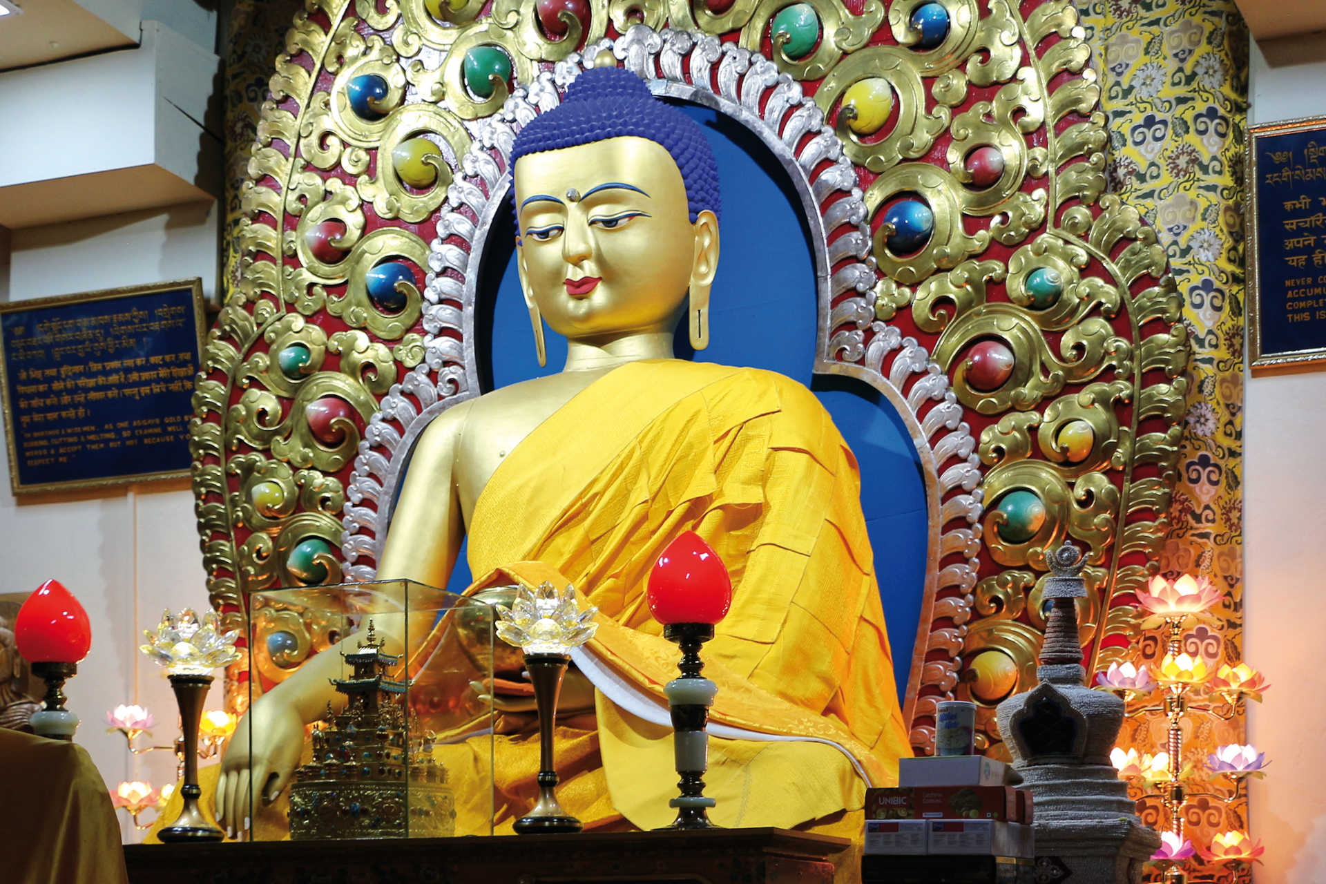 Goldene Buddha-Statue mit gelber Robe und farbenprächtigem Schmuckrahmen in Bodhgaya