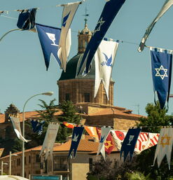 Bunte Fahnen und Banner hängen über einer Straße mit Kirchturm