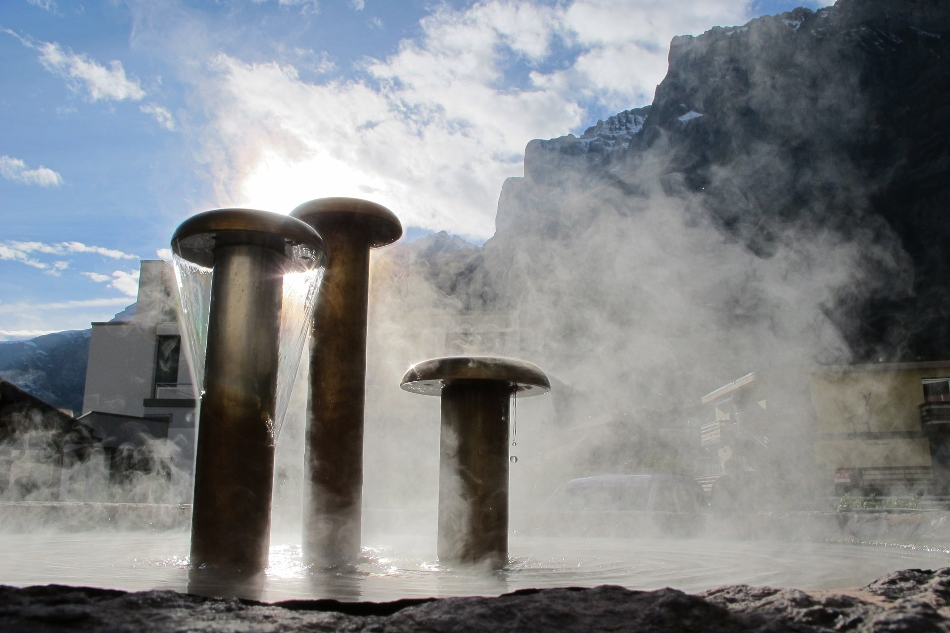 Aufsteigender Dampf über Thermalbrunnen in Bergkulisse