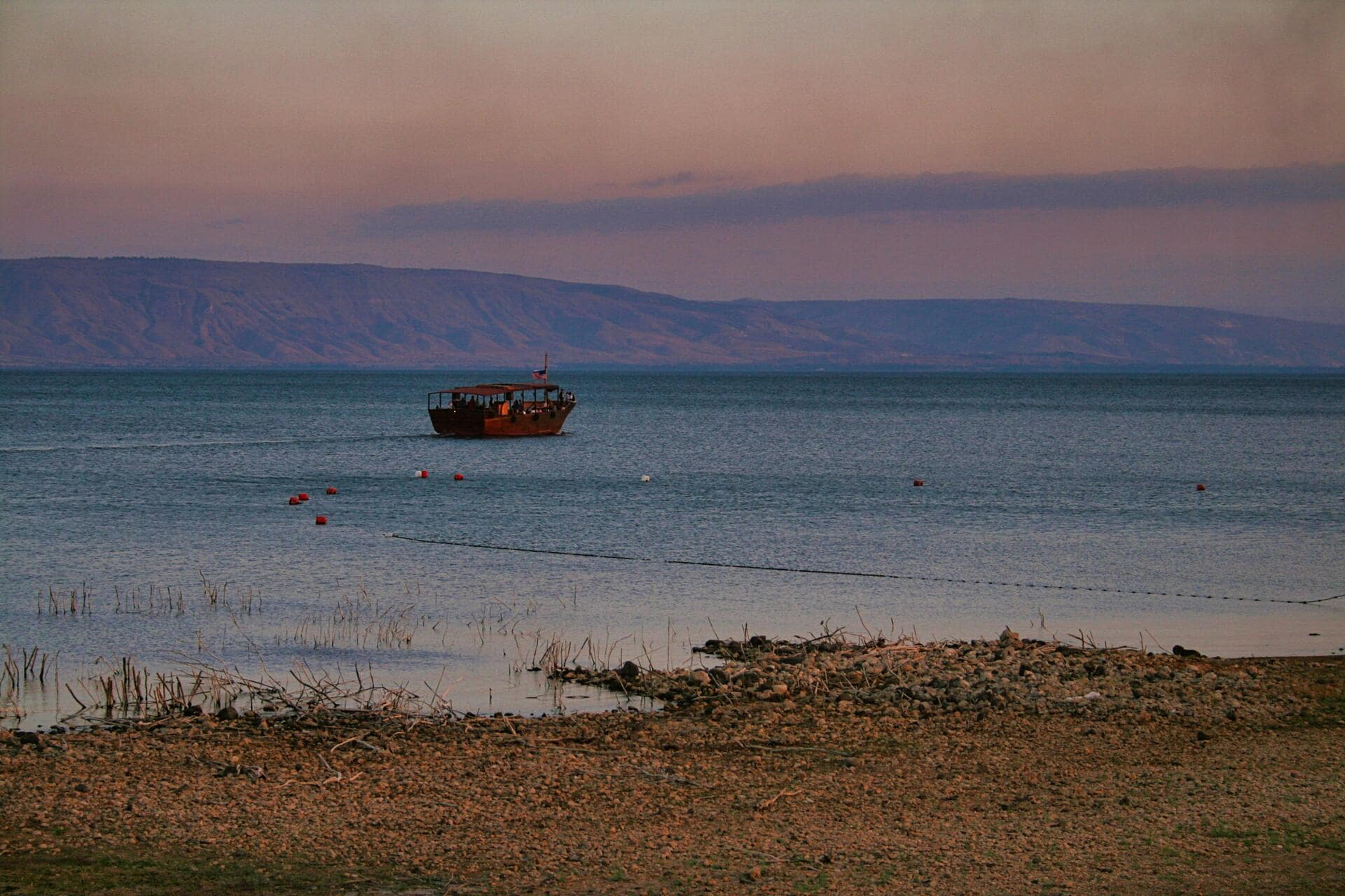 Kleines Holzboot auf ruhigem See vor Hügeln bei Abenddämmerung