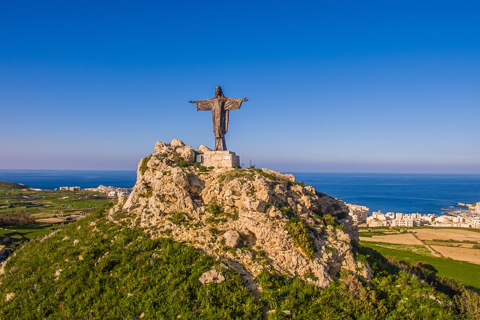 Panoramablick auf die Christusstatue auf einem Hügel bei Marsalforn mit Küste im Hintergrund