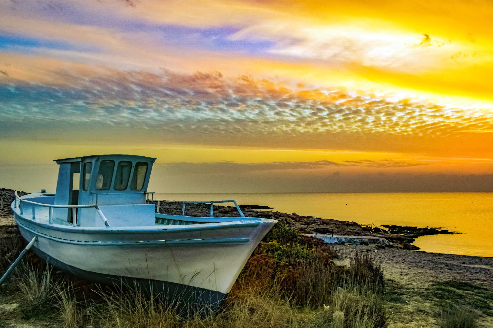 Kleines Boot auf Land vor dem Meer bei farbenprächtigem Sonnenuntergang