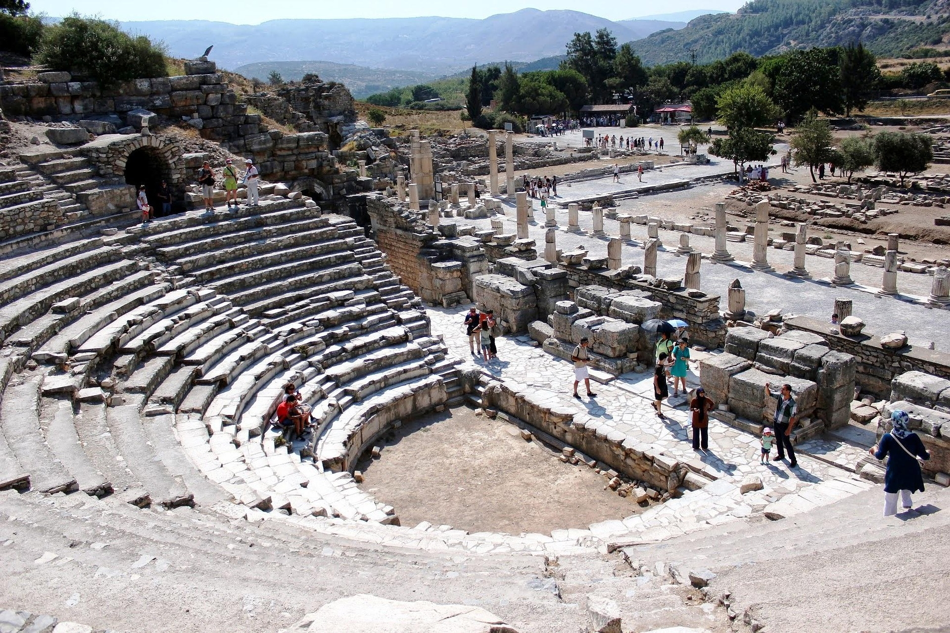 Halbrundes antikes Theater mit Ruinen und Besuchern im Sonnenschein