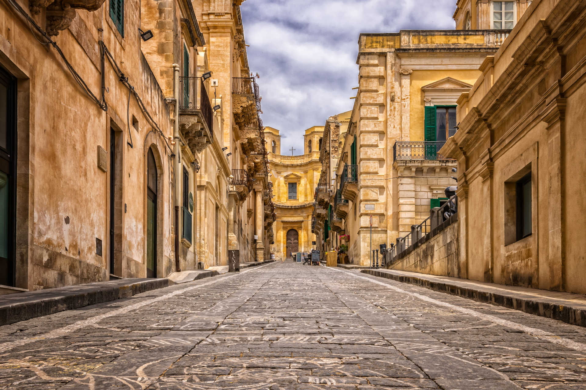 Blick entlang einer gepflasterten Straße in der Altstadt von Noto auf Sizilien mit reich verzierten Barockfassaden aus hellem Sandstein.