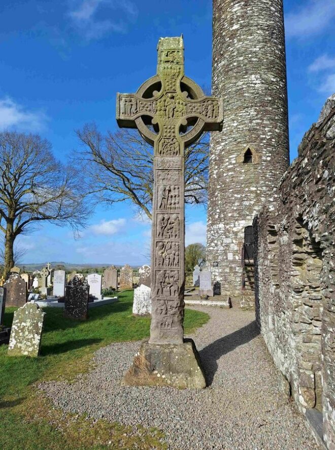Verziertes Hochkreuz aus Sandstein vor dem Rundturm der Klosterruine Monasterboice, Irland