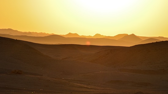Sonnenuntergang über sanften Dünen und fernen Bergsilhouetten