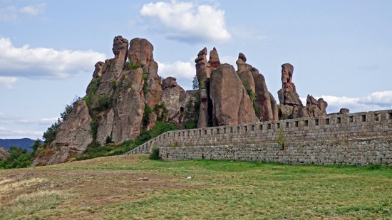 Hohe rote Felsen ragen hinter alter Steinmauer in den Himmel