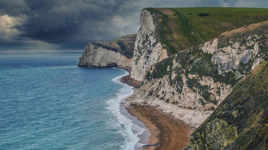 Hohe weiße Klippen fallen steil zum Meer unter dunklen Wolken ab