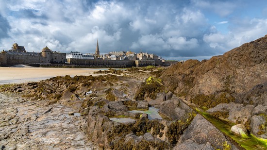 Blick über Felsen auf historische Stadtmauer mit Kirchturm am Meer
