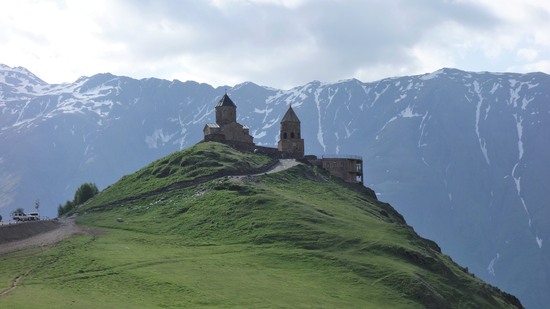 Alte Kirche thront auf grünem Hügel vor schneebedeckten Gipfeln