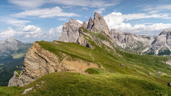 Grüne Berghänge führen zu schroffen spitzen Felsen unter blauem Himmel
