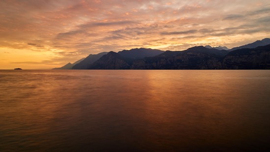 Berge spiegeln sich im ruhigen Wasser unter goldenem Abendhimmel