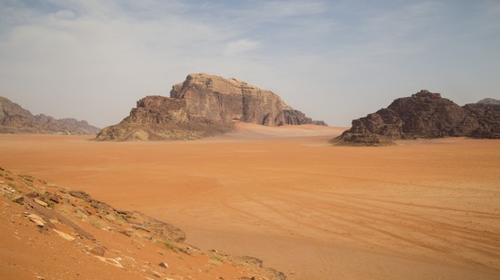 Weite Sandfläche mit markanten Felsformationen unter blauem Himmel