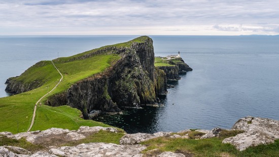 Grüner Felsen ragt ins Meer hinaus mit Leuchtturm an der Spitze
