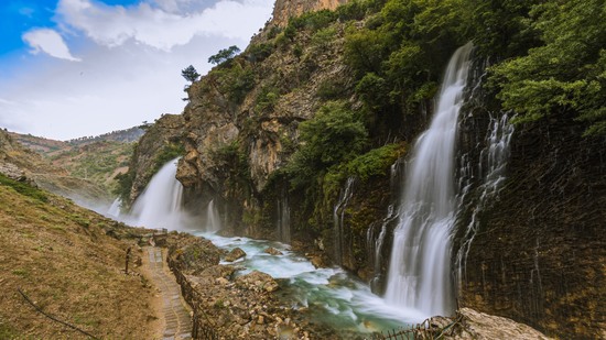 Mehrere Wasserfälle stürzen an Felswänden in einen Gebirgsbach