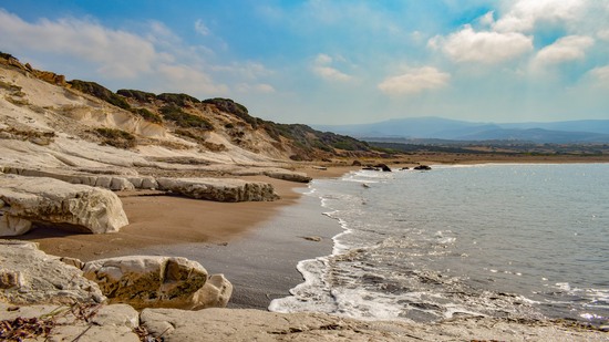 Sanfte Wellen am Sandstrand mit Felsen und Hügeln im Hintergrund